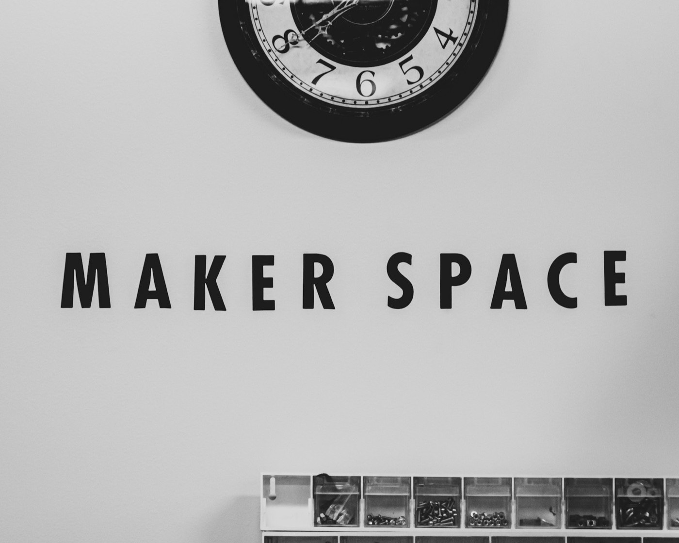 A makerspace sign on the wall above a rack of parts bins