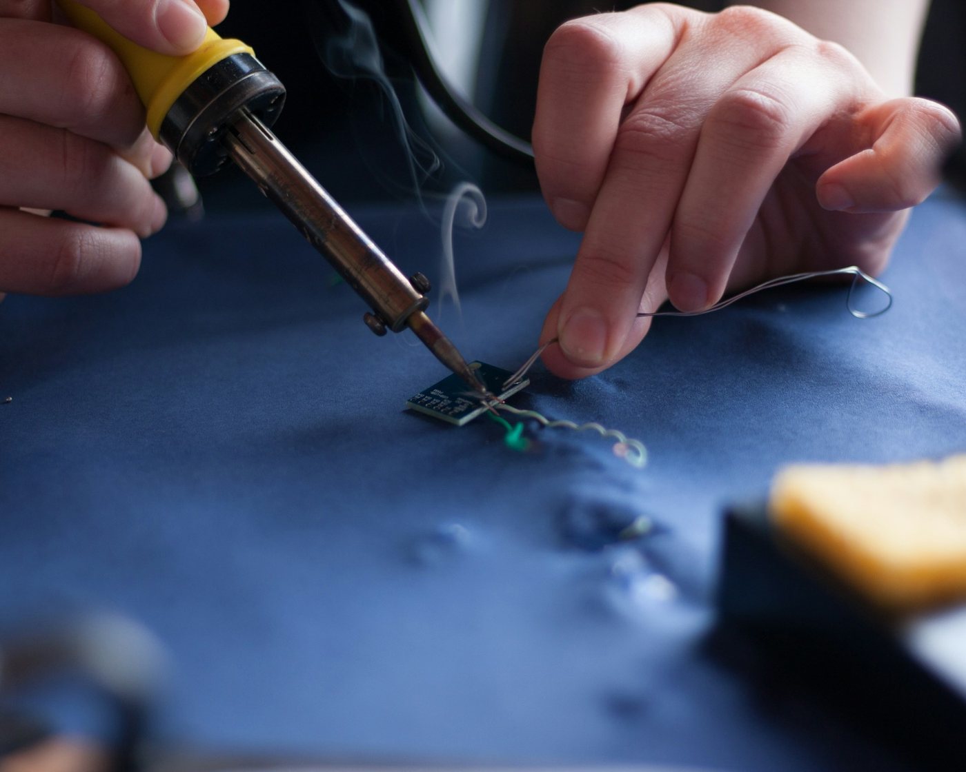 Hands soldering a wire onto a small circuit board